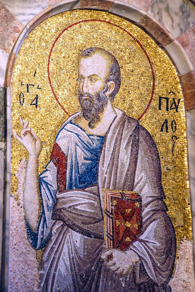 Mosaic of a figure with a beard and halo, wearing a robe, gesturing with one hand while holding a book in the other.